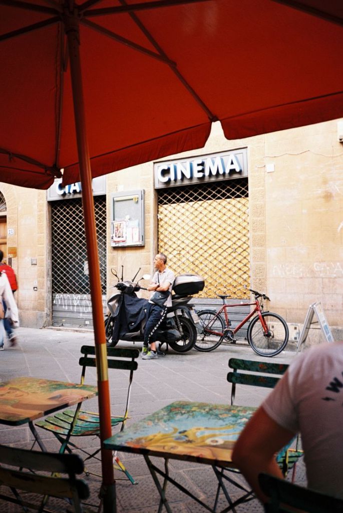 Mann vor einem alten Kino in Italien an seinem Motorrad wartend